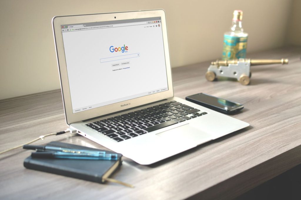 The Art of Drawing Readers In: Your attractive post title goes here A neat workspace featuring a laptop displaying Google search, a smartphone, and a notebook on a wooden desk.