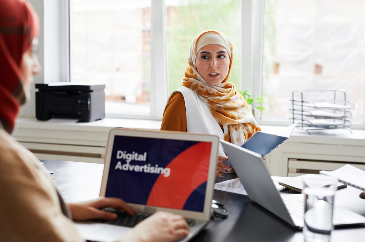 service-02 Two women in hijabs discuss digital advertising in an office setting.